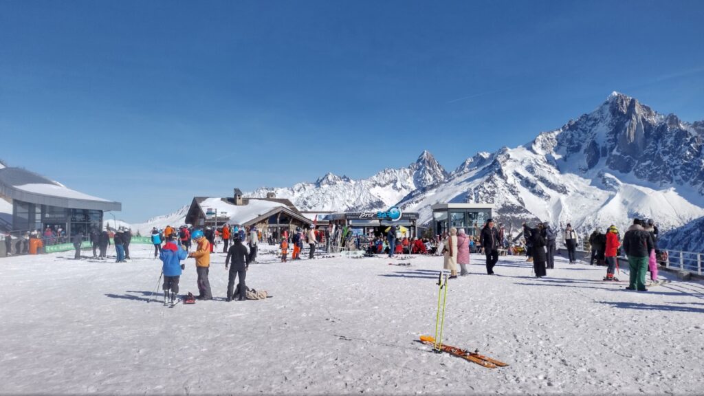Lots of skiers and tourists with mountains in the background