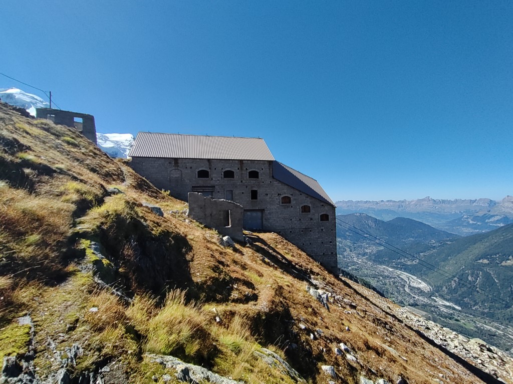 Gare des Glaciers - another large abandoned granite building on a sunny hillside with mountains in the background
